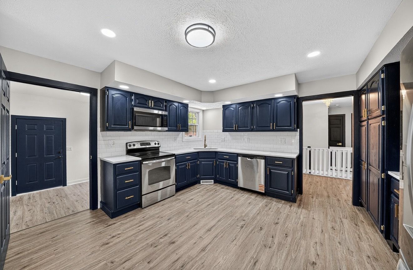 Completed kitchen remodel with navy cabinets, white subway tile, gold hardware, and LVP flooring